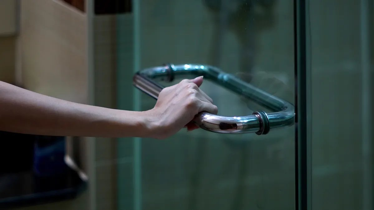 A person adjusting a dimmer switch in a bathroom, illustrating the intentional control over light for a dark showering experience.