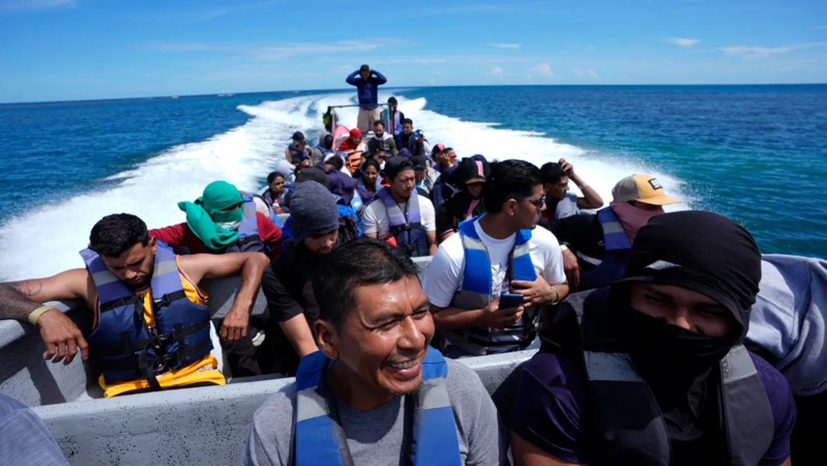 A man with a weary expression sits on a beach, surrounded by bags.