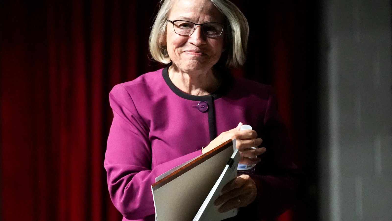 Representative Thompson standing at a podium, addressing a town hall audience, his expression serious and engaged during a question-and-answer session.