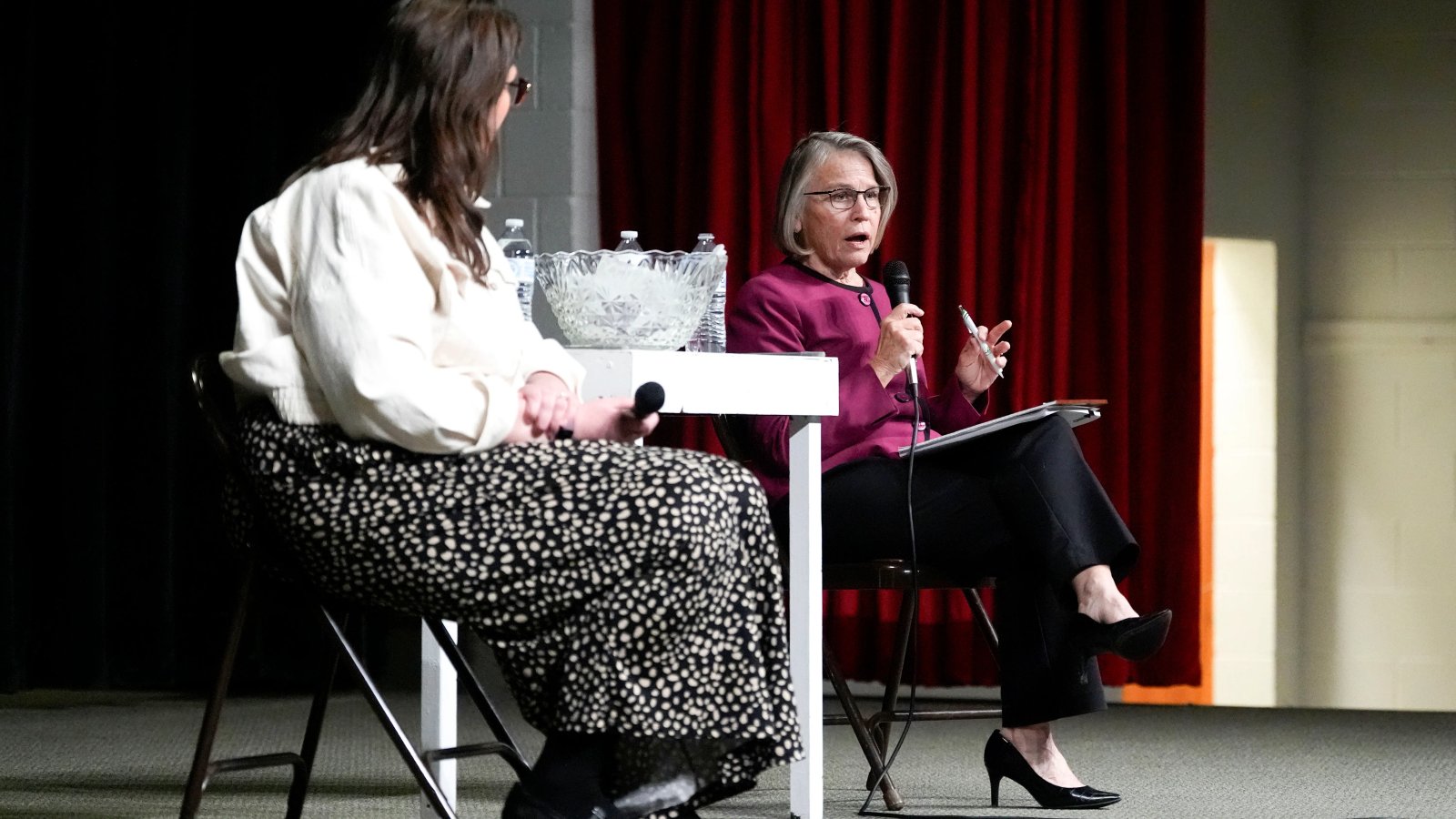 A male town hall attendee passionately speaking into a microphone, surrounded by a diverse audience.