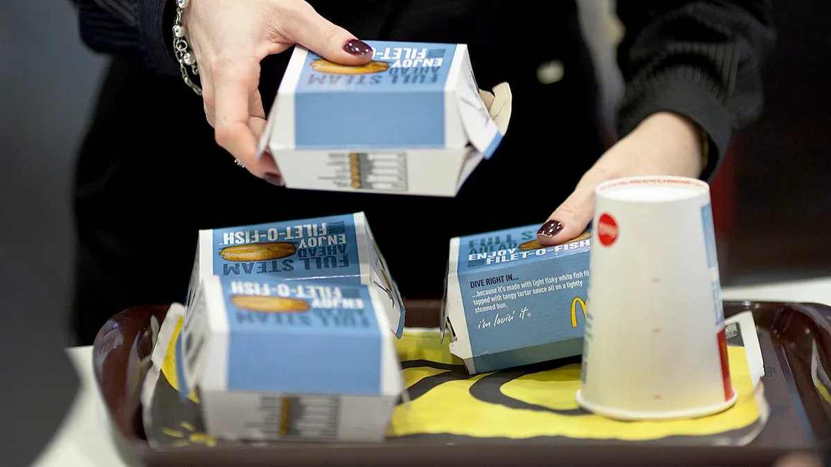 A McDonald's employee handing a Filet-O-Fish to a customer at a drive-thru window.