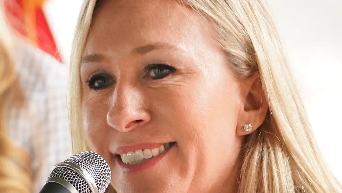 Marjorie Taylor Greene speaking passionately at a political rally, supporters in the background.