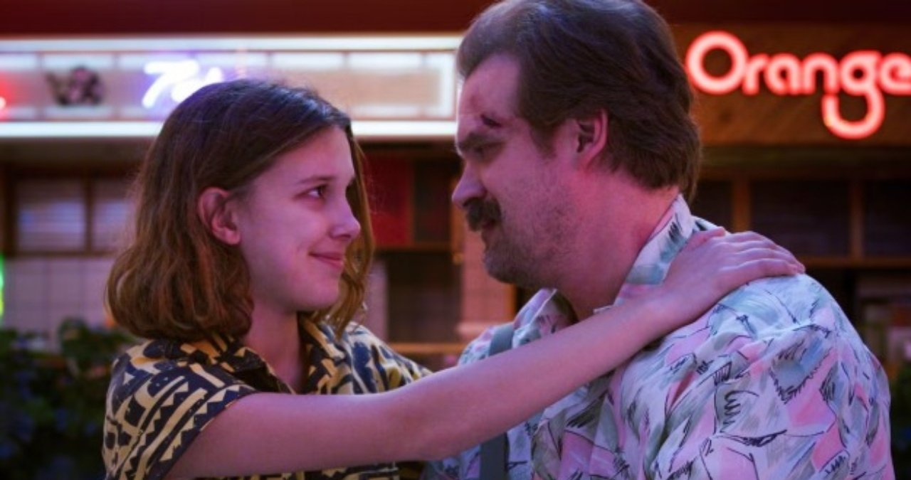 Millie Bobby Brown and David Harbour smiling together at an event.
