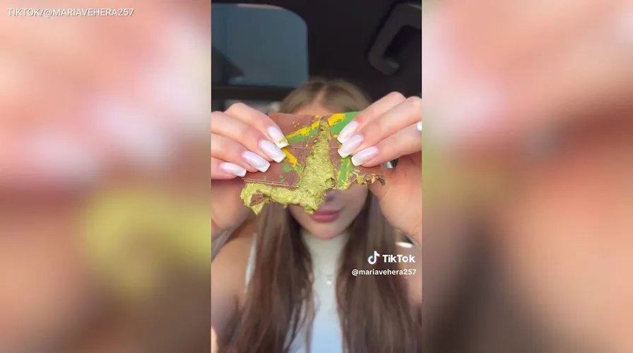 A person holding a small piece of dark chocolate, about to take a bite, with a thoughtful expression.