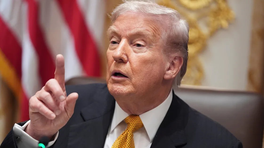 A CNN host pointing to a screen displaying economic data charts during a live broadcast, with a serious expression.