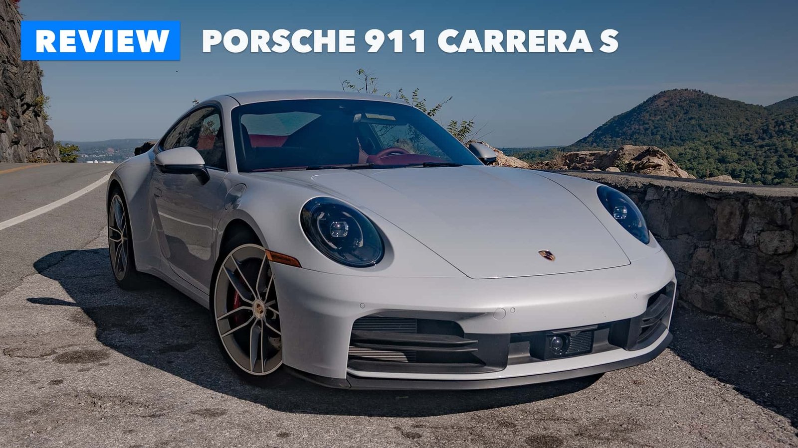 A vibrant blue Porsche 911 Carrera S parked on a scenic coastal road, highlighting its sleek design and sporty stance.