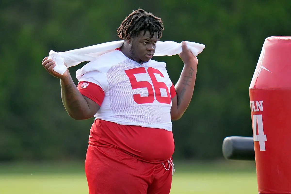Desmond Watson, a large defensive tackle, stands on a football field in a Buccaneers uniform, looking determined.