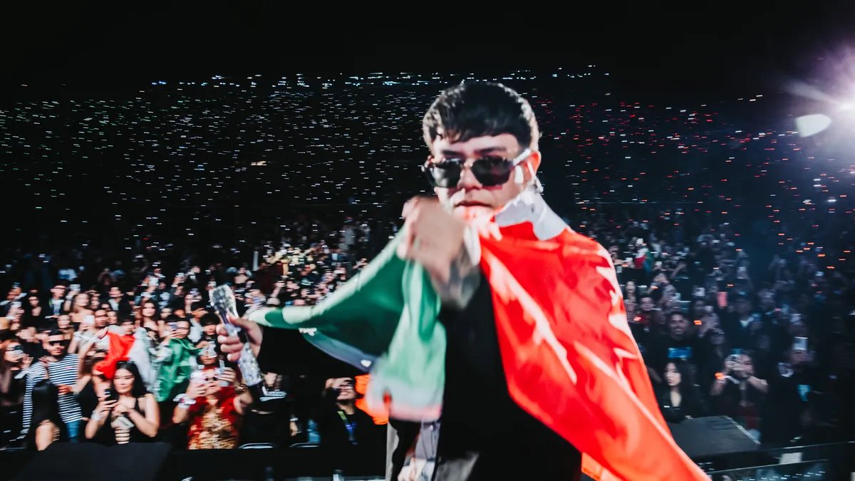 Mateo 'El Fénix' Ramirez performing live in a packed arena, bathed in spotlights.