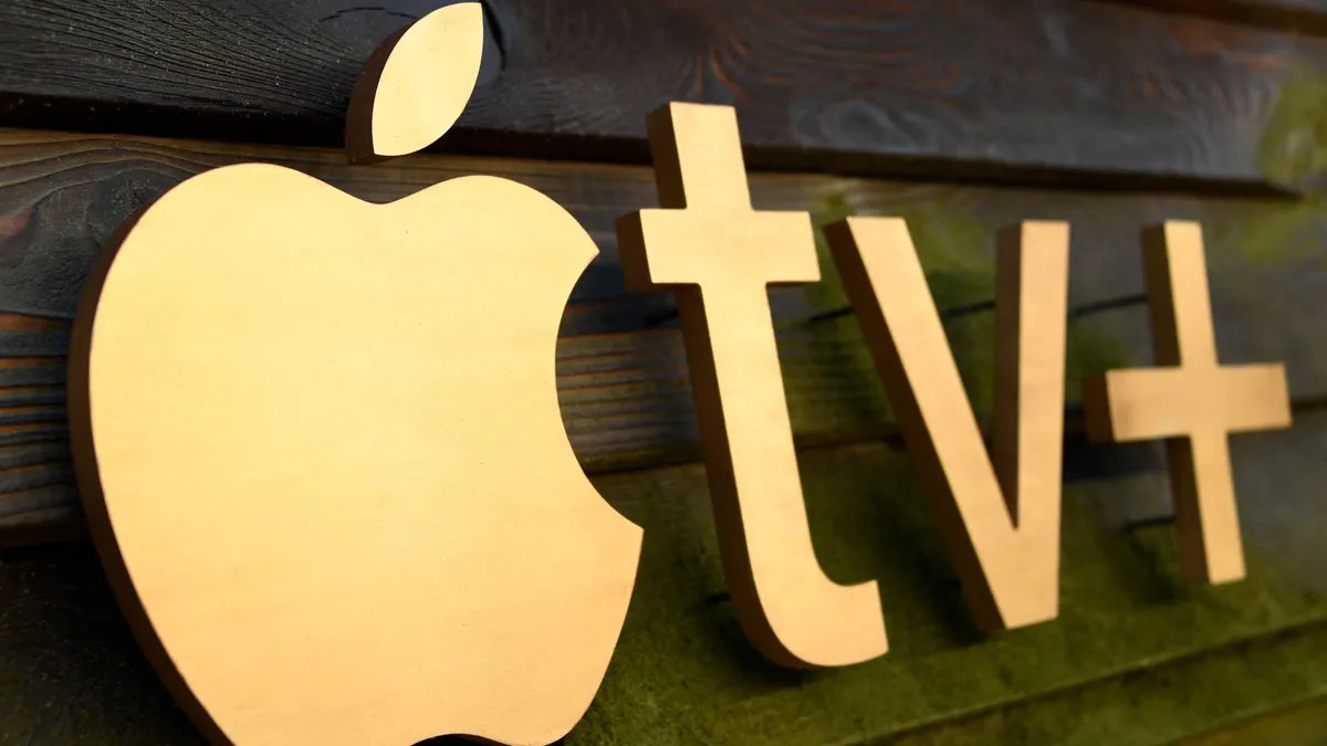 Apple TV+ logo against a blurry background of studio lights and equipment.