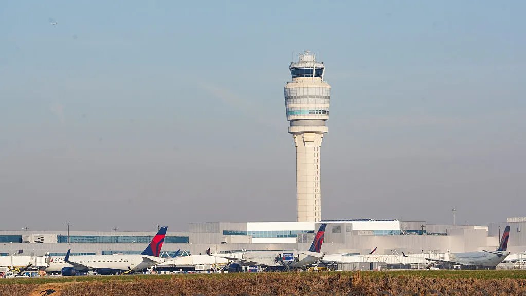 A frustrated traveler looks at a departures board showing multiple flight delays and cancellations at an airport.