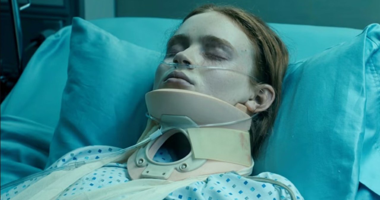 Max Mayfield in a hospital bed, surrounded by medical equipment, her eyes closed, suggesting her comatose state.