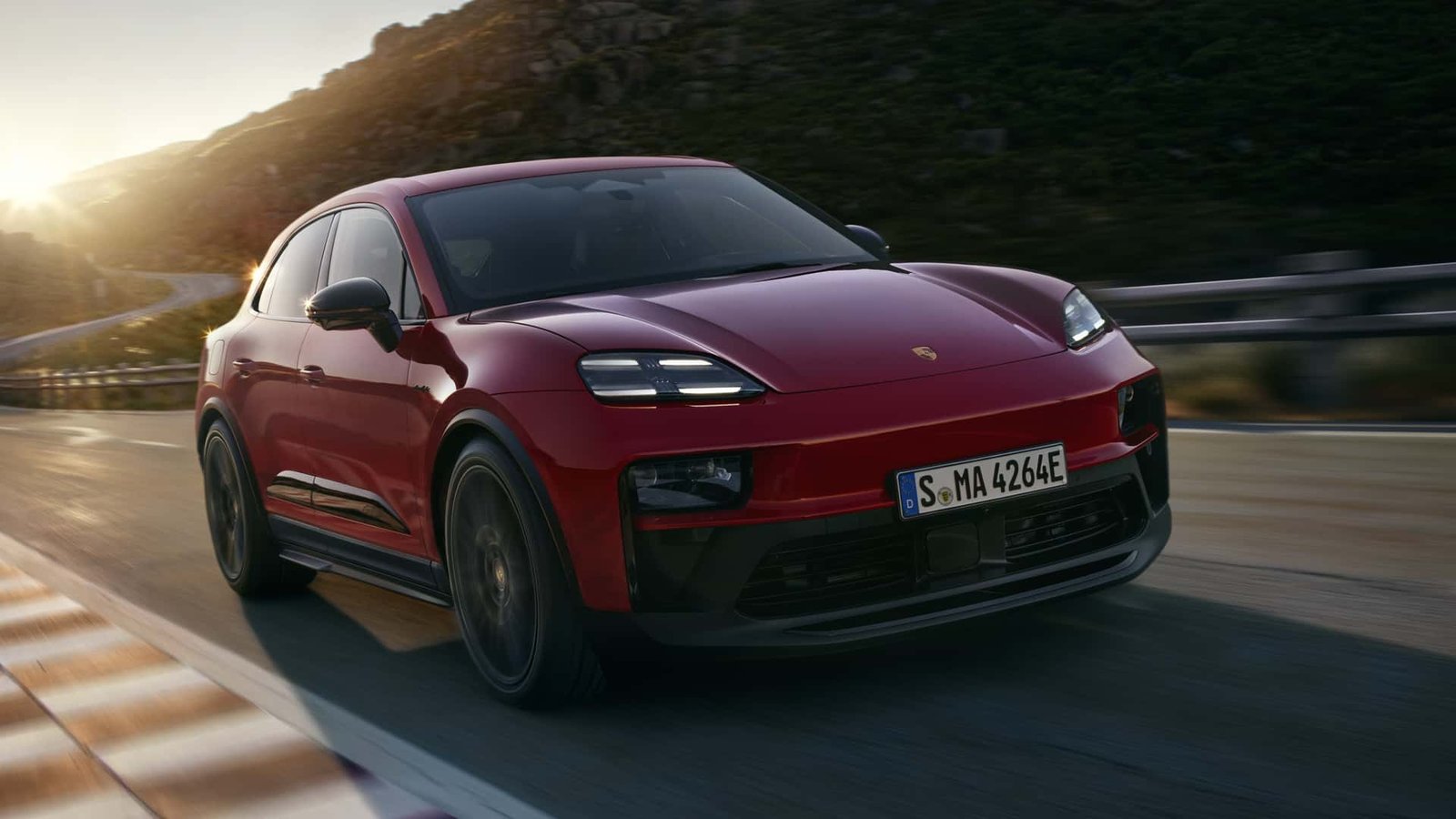 A sleek, red Porsche Macan GTS, fully electric, parked on a winding road, showcasing its aggressive styling and modern design.