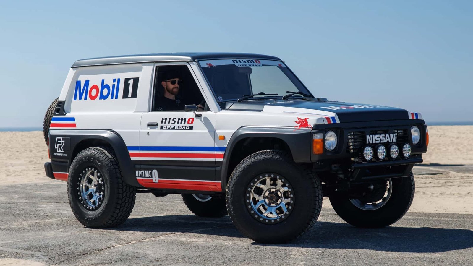 A highly modified, gleaming white Nissan Patrol aggressively posed on an off-road track, showcasing its powerful stance.