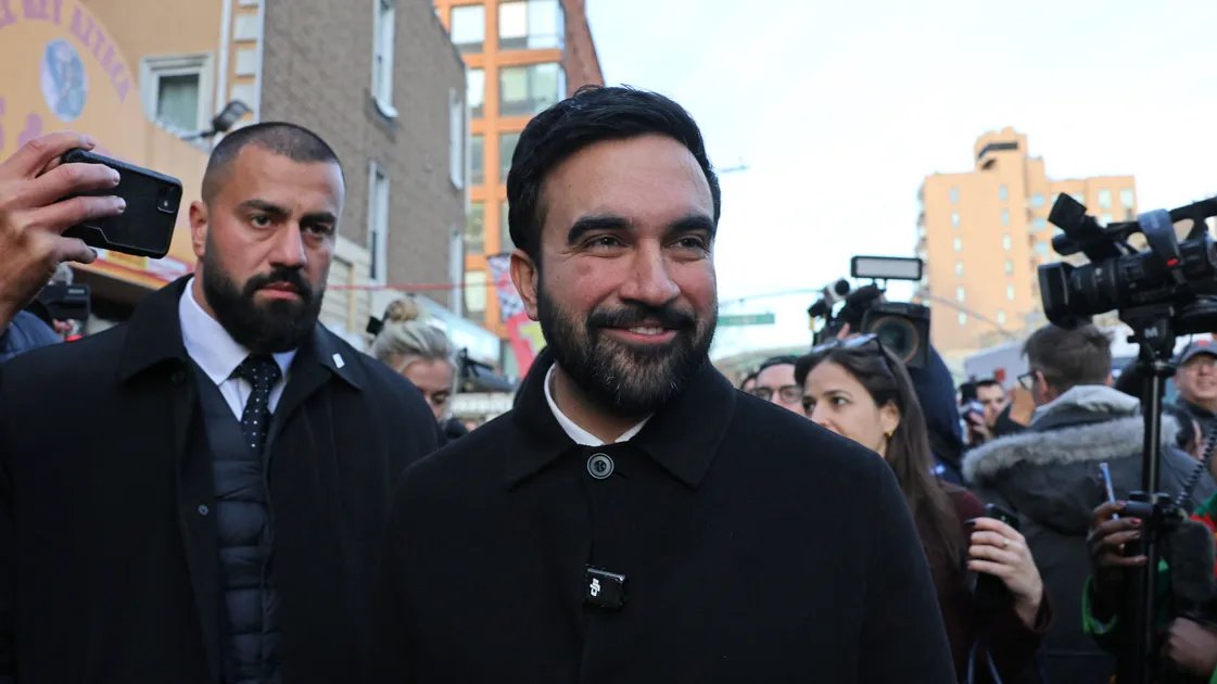 Zohran Mamdani stands with striking Starbucks workers, holding a sign in support of their unionization efforts.