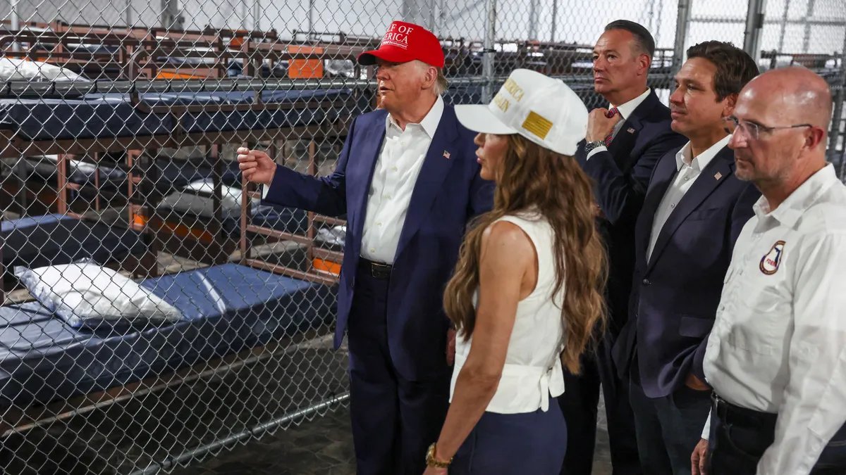 A somber, imposing view of the Alligator Alcatraz facility, with high walls and watchtowers, shrouded in a morning mist.
