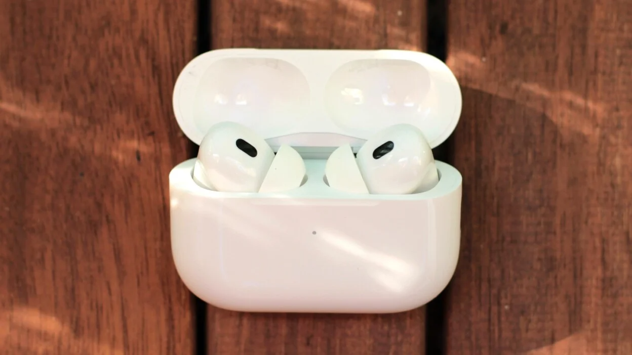 A pair of white Apple AirPods Pro earbuds in their charging case, with a blurred background suggesting a variety of potential color options.