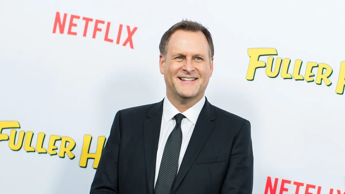 Dave Coulier in his early stand-up days, microphone in hand, telling a joke on stage.