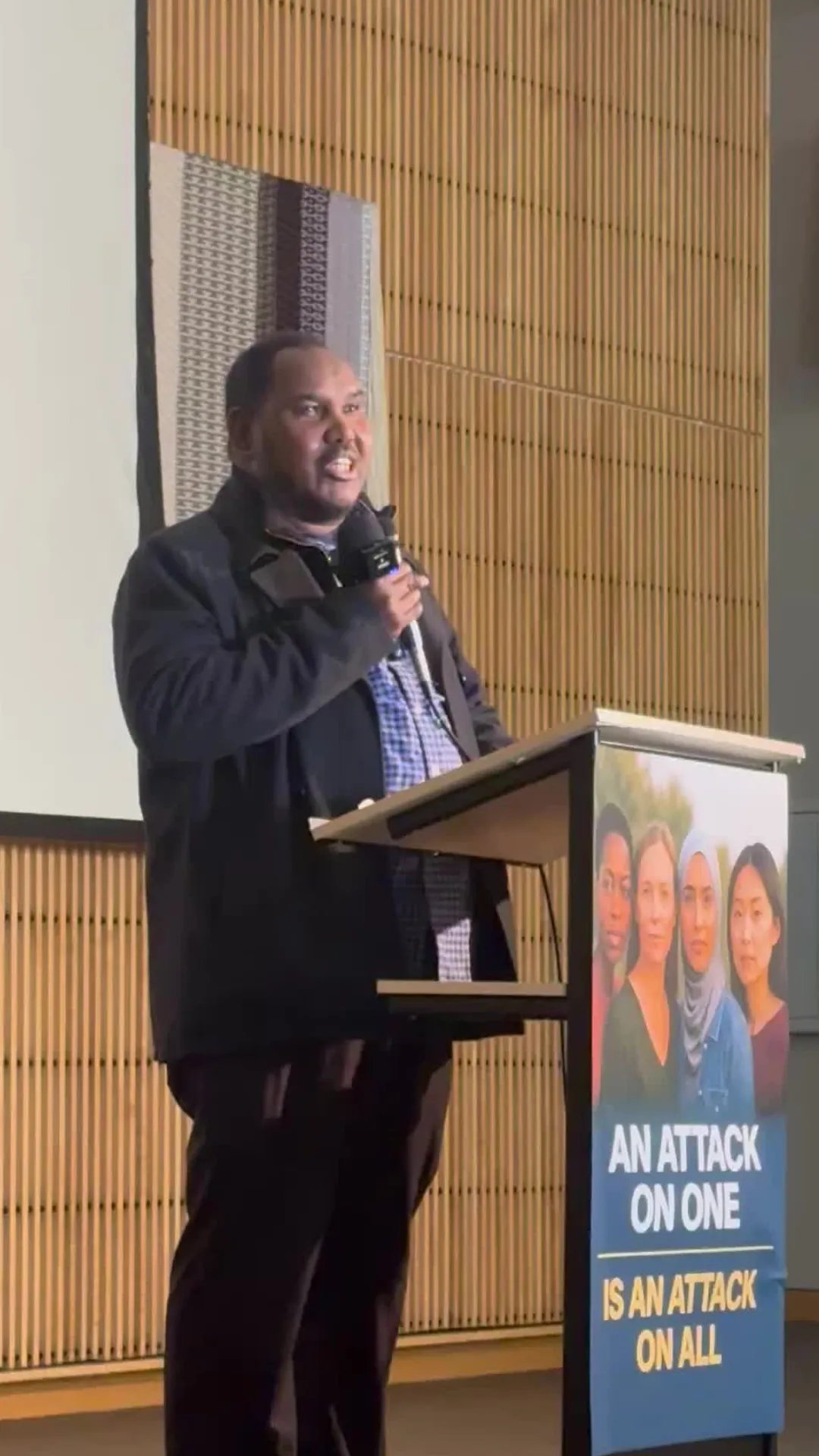 A Somali-American man speaking passionately at a community meeting in Minneapolis, gesturing with his hands.