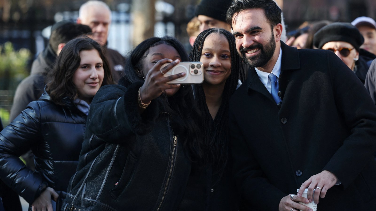 A determined woman shouting passionately at a political rally, surrounded by a crowd with similar expressions of strong conviction and frustration. The blurred background suggests a large, engaged gathering.