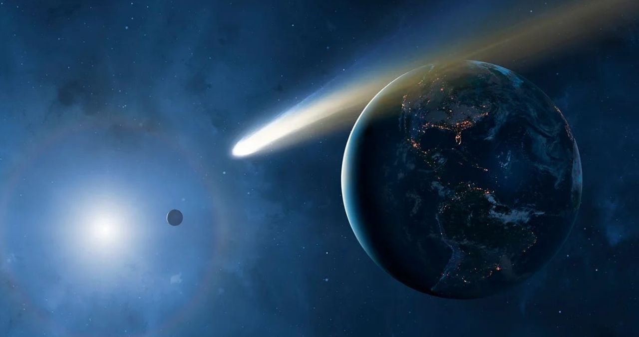 A vibrant, long-exposure image of a comet with a bright nucleus and a long, flowing tail, set against a star-filled dark sky. The comet appears to be moving from left to right.