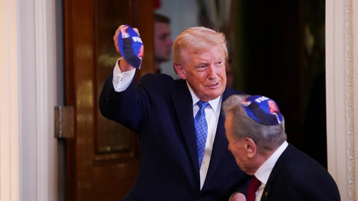 Donald Trump addressing a diverse group of guests at a festive White House Hanukkah celebration, with a large menorah visible in the background.