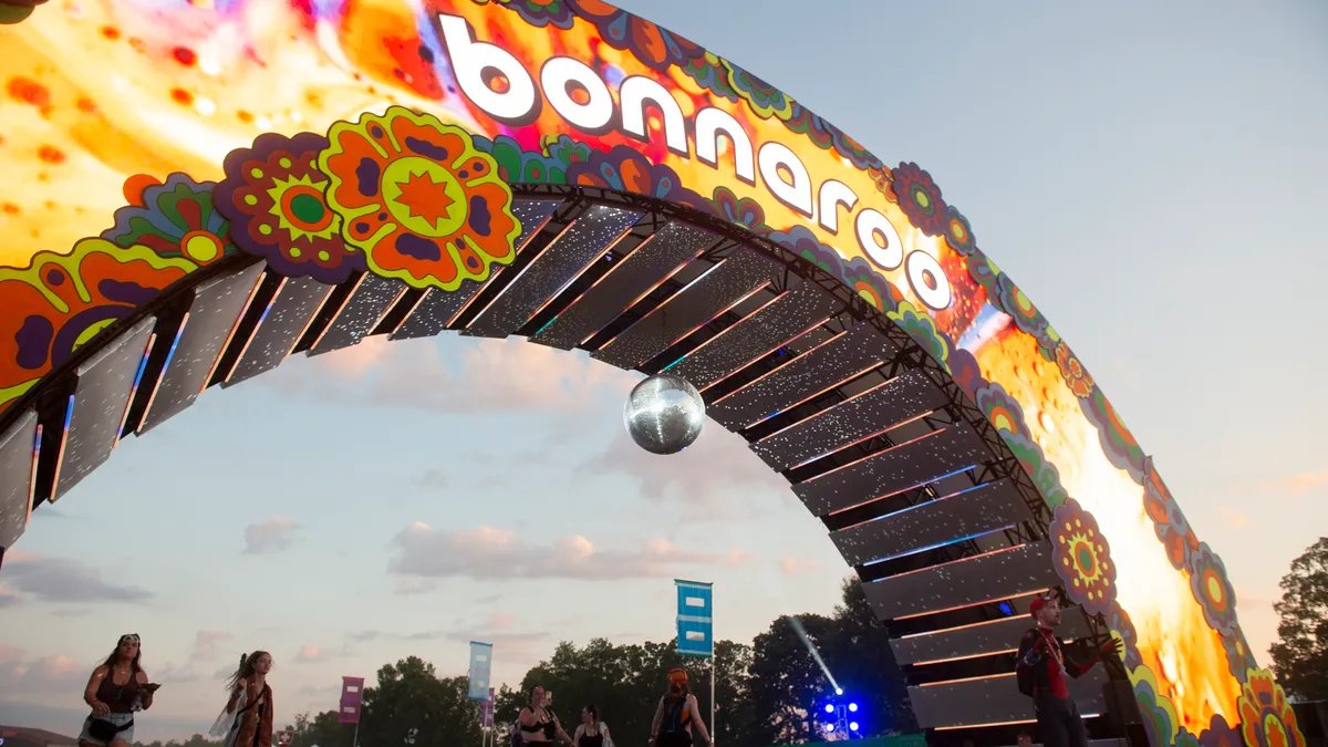 Bonnaroo festival crowd silhouetted against a colorful sunset.