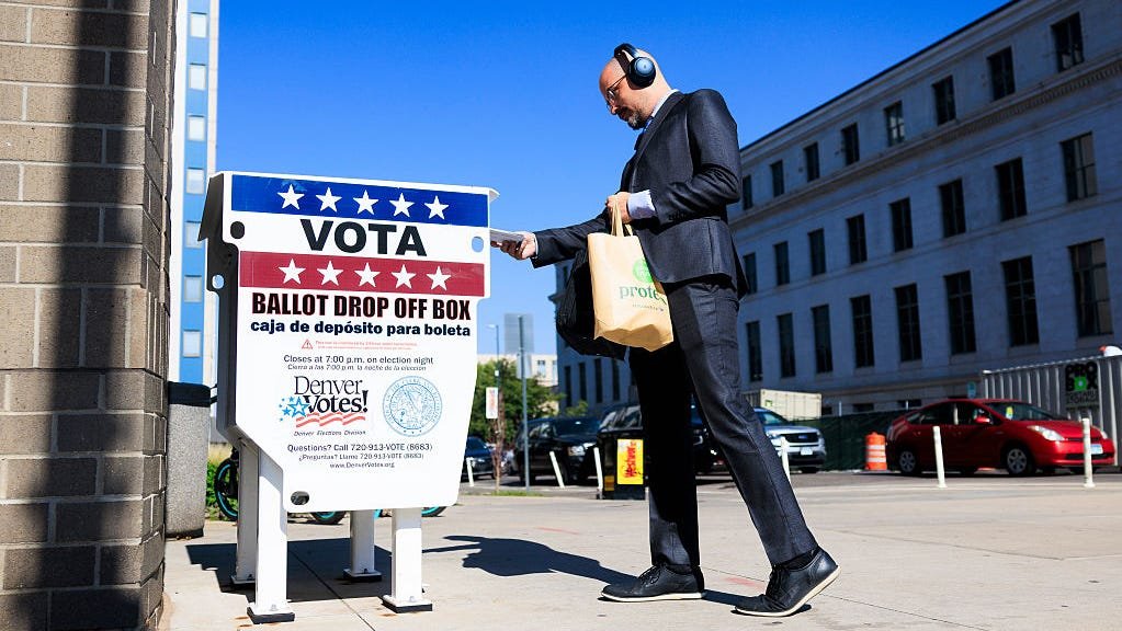 Voter placing mail-in ballot in drop box during election Voter placing mail-in ballot in drop box during election